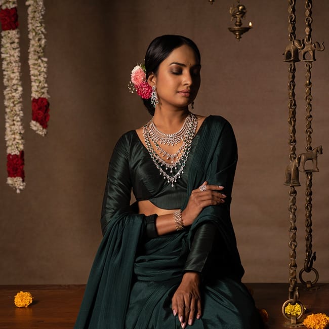 A bride draped in a saree poses with stunning bridal diamond layered necklaces, diamond bangles, a diamond ring, and diamond earrings suitable for weddings.
