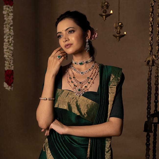 The bride poses with layered diamond necklaces, diamond earrings, and a diamond ring with green gemstones. She also wears diamond bangles to match her bridal outfit.