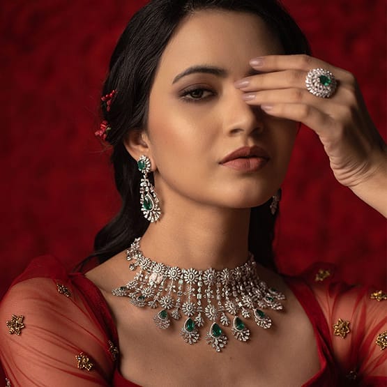 A female model is wearing a diamond necklace with a beautiful earrings and ring with a emerald stones.